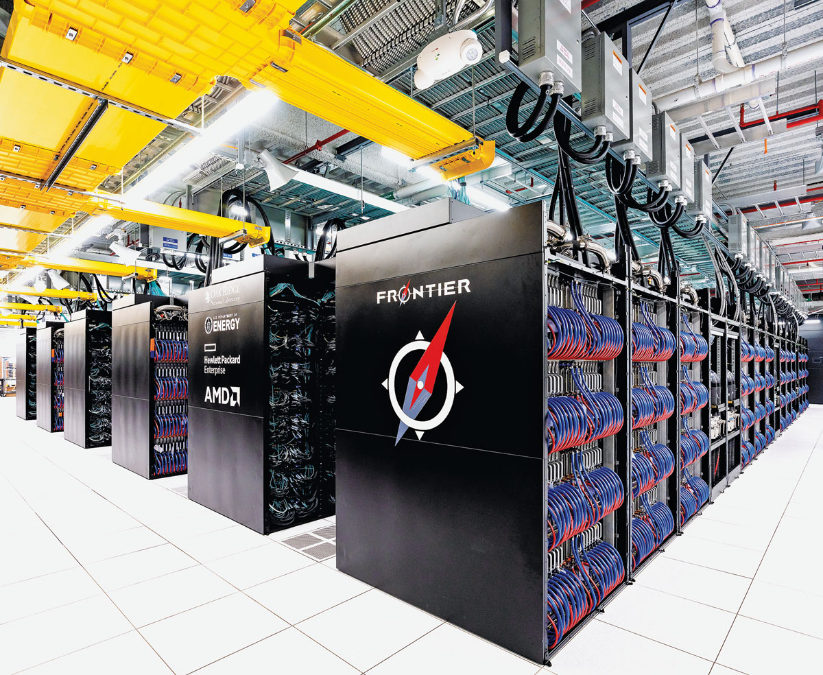 A view looking at one corner of a the Frontier supercomputer. The machine's black cabinets receed into the background in a bright, white room. The back of the cabinets has been removed to show red and blue hoses.