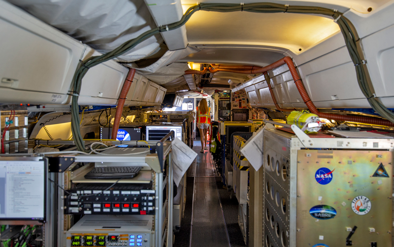 A view of the inside of an aircraft with racks of equipment to either side of an aisle.