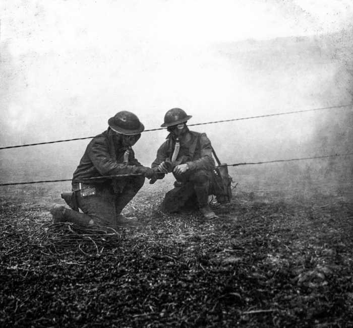Soldiers repair a telephone wire while surrounded by poison gas during training.